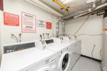 A laundry room with washers and dryers and warning signs on the wall.